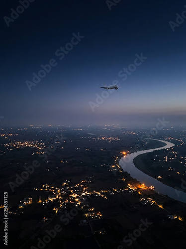 Commercial aircraft flying over illuminated city at dusk with river