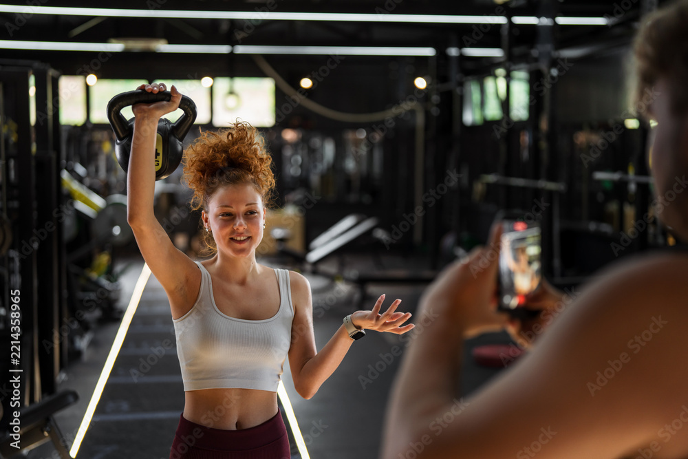 Naklejka premium Woman influencer creating fitness content with kettlebell in gym