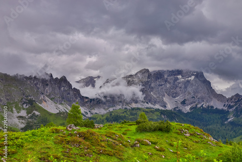Panoramic alpine landscape around Salzburg, Austria, featuring majestic snow-covered peaks, rugged mountain ridges, green foothills, forested slopes, and picturesque valleys of Austria