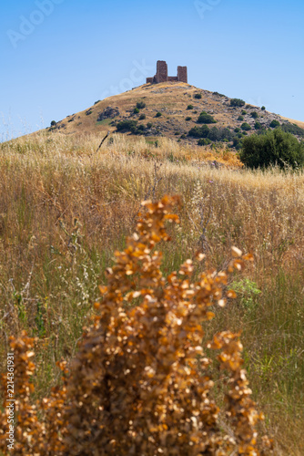 Obraz na plátně Weathered stone fortress ruins stand atop a sun-scorched hill surrounded by sparse scrubby vegetation