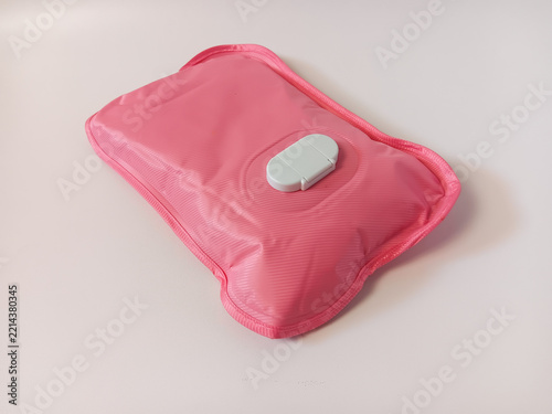 Close up of a pink rechargeable electric hot water bag (or electric heating pad) with a soft-touch ribbed PVC surface and a central charging port cover, used for soothing warmth and muscle relief isol