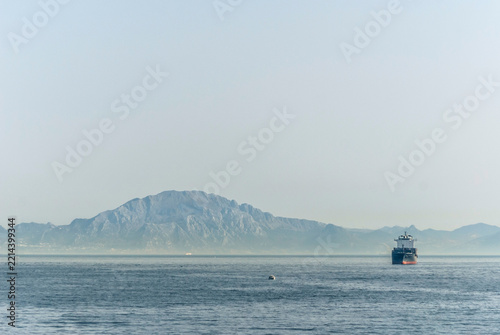 Cargo ship sailing near the Rock of Gibraltar with Jebel Musa of Rif Mountains in Morocco, Africa in the background