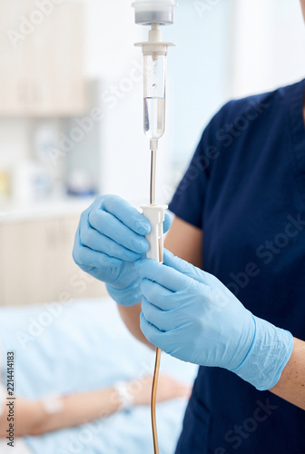 Nurse adjusting IV drip with gloved hands in a hospital room  