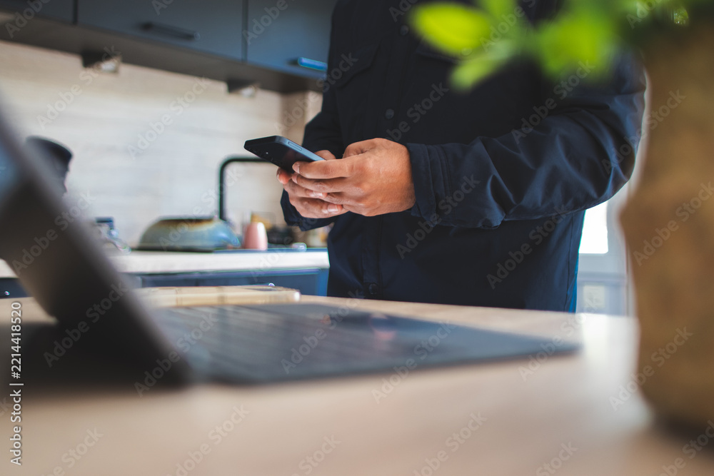 Fototapeta premium Person holding smartphone while working from home, staying connected and managing tasks in a modern kitchen, balancing personal and professional life