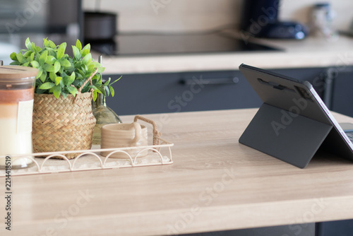 Wooden kitchen counter with a tablet standing beside a decorative tray holding a potted plant, candle and ceramic cup, creating a cozy, minimalist tech ready workspace