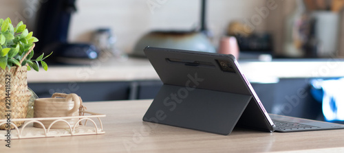 Modern tablet with keyboard case on a wooden kitchen countertop, showcasing contemporary technology and comfortable work from home or smart living setup