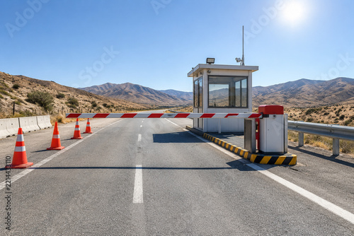 Empty road checkpoint with lowered red and white barrier arm, guard booth and cones, security and traffic control concept