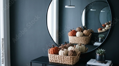 Autumn and Halloween decorations arranged on a console table beneath a round mirror in a modern entryway. Woven baskets and pumpkins create a warm seasonal welcome.