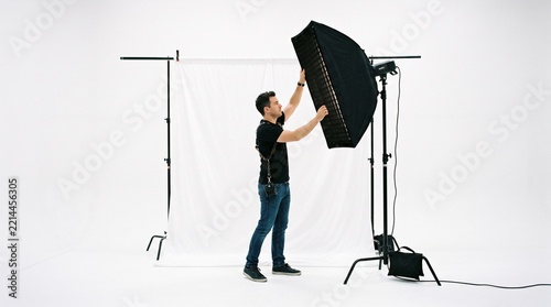 Photographer adjusting a large softbox light modifier in a professional studio with a white backdrop