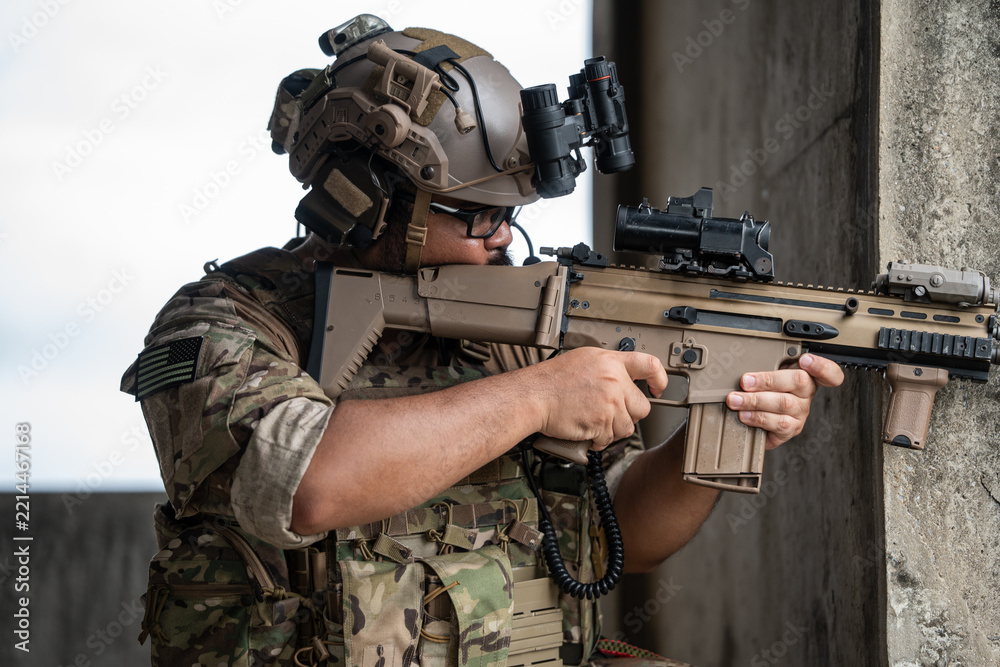 Fototapeta premium A tactical soldier holds a modern rifle with intense focus while aiming around a concrete corner, conveying a sense of vigilance, readiness, and strategic defense.