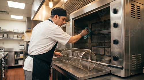 Chef cleaning inside of rotisserie oven in professional kitchen  
