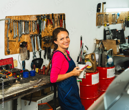 Candid portrait pop female auto mechanic with smartphone during coffee break at work in a local auto repair shop