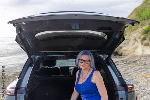 Woman is sitting in the trunk of her car by the seaside. Travel concept. Horizontally. 