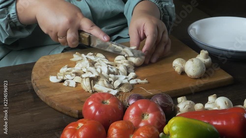 A woman's hands slice champignons with a knife on a cutting board on a table