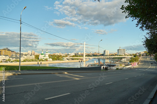 Tyumen, Russia - September 6, 2026: Wide urban landscape showing Tura River embankment, cable stayed Bridge of Lovers, Church of All Saints, and city street