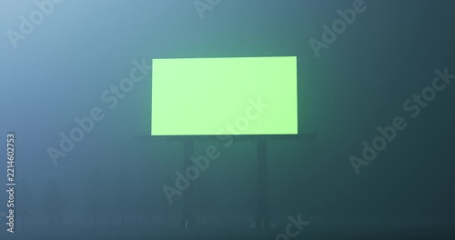 Camera slowly approaching blank glowing green screen billboard standing in dark foggy night