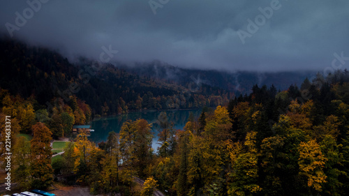 Scenic autumn landscape of Alpsee lake surrounded by colorful forest and foggy mountains in Bavaria, Germany