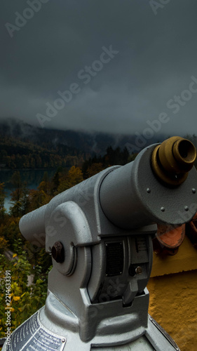 Tourist viewing telescope at Hohenschwangau viewpoint over foggy mountains and lake, Bavaria