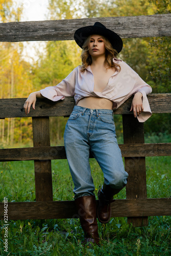 Woman in a pink shirt and black hat posing against a fence