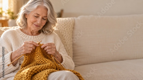 Senior woman knitting a mustard yellow blanket on a comfortable sofa