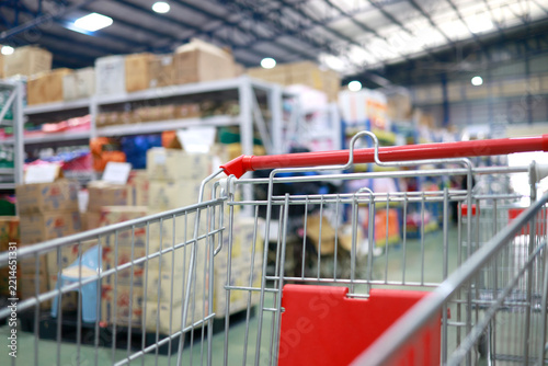 Empty shopping cart inside a large retail store, with blurred shelves and cardboard boxes in the background, shopping, wholesale, retail business and consumer lifestyle