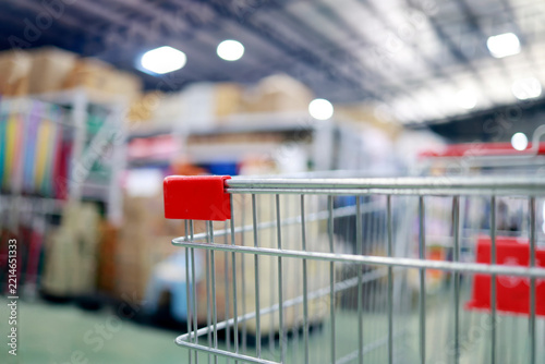 Empty shopping cart inside a large retail store, with blurred shelves and cardboard boxes in the background, shopping, wholesale, retail business and consumer lifestyle