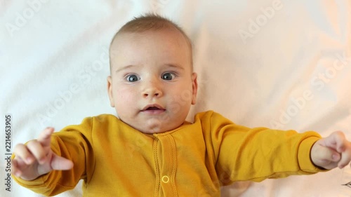 Beautiful, cute baby looks at the camera and smiles happily, waving its little hands.