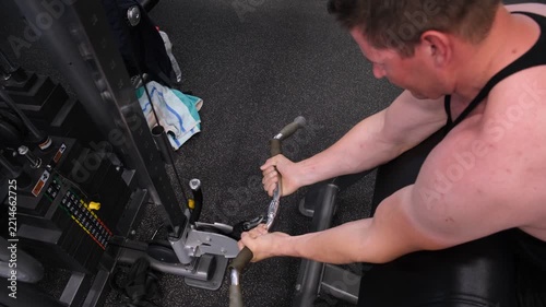 Muscular man adjusting a cable machine attachment in a modern gym, concept of strength training, workout preparation, bodybuilding, fitness routine, exercise equipment, discipline and active lifestyle