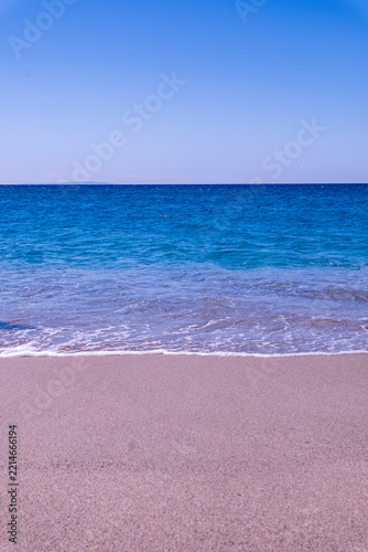 Blue sea meeting empty sandy beach under clear sky