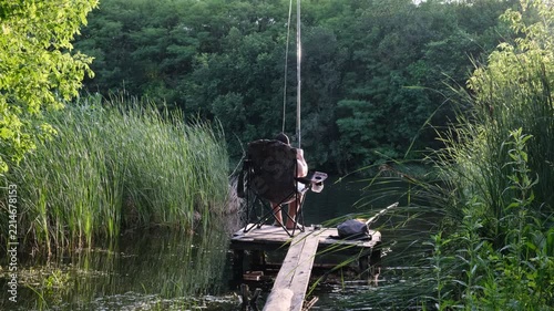 Man casting a fishing rod from a narrow wooden pier surrounded by reeds, concept of recreational fishing, angling, solitude, rural leisure, freshwater ecosystem, poaching awareness and illegal fishing