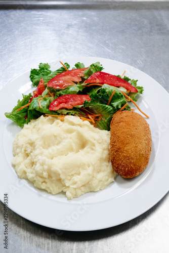 Fotografie Creamy mashed potatoes served with a golden breaded croquette and a fresh tomato and lettuce salad on a white plate, ideal for lunch or dinner menus and comfort food photography