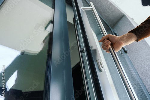 Man's hand opening modern aluminum entrance door with stainless steel handle