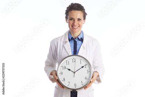 A smiling healthcare professional in a lab coat holding a wall clock, representing time management, appointment scheduling, and patient waiting times.