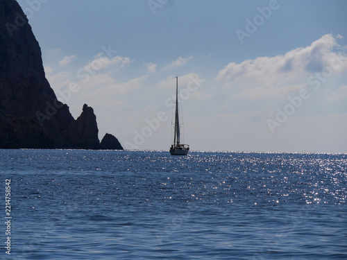 Lone sailboat silhouetted against dramatic rocky peak in Mediterranean Corsica