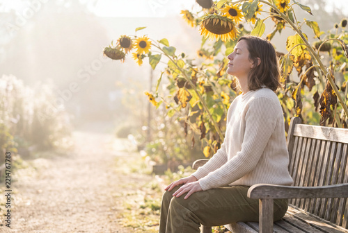Woman Sitting On Wooden Bench Surrounded By Blooming Sunflowers In Autumn Garden