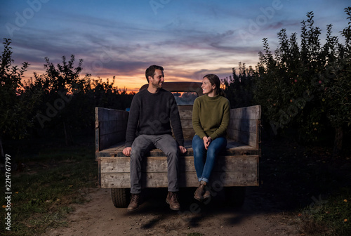 Romantic Couple Relaxing On Vintage Pickup Truck In Orchard At Sunset