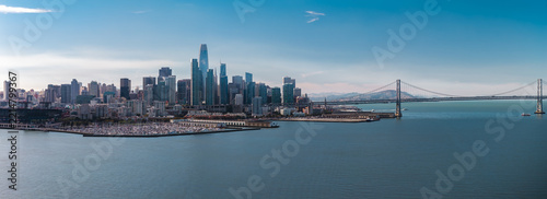 Aerial wide view of San Francisco downtown skyscrapers, Salesforce Tower, marina harbour, and the Oakland Bay Bridge spanning over the calm bay water on a clear day.