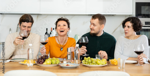 Couple are sitting at table with friends, drinking wine and enjoying snacks, chatting merrily, raise glass to, celebrating important event.
