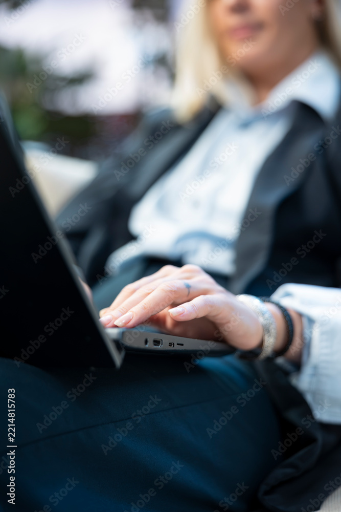 Fototapeta premium Close-up shows a woman's hand using a laptop touchpad and typing during outdoor work, with a black business suit and a remote workspace setting.