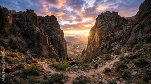 Hiker walking on desert trail at sunset between towering rock formations