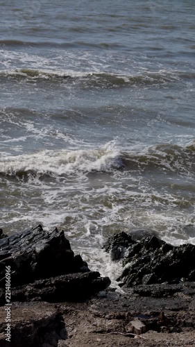 Waves Breaking Over Dark Coastal Rocks Along Gritty Shoreline in Gray Open Water