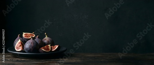 Bodegón de estilo clásico con fondo oscuro de higos enteros y cortados sobre palto negro, horizontal banner, con espacio negativo.