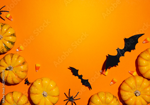 Halloween background texture with mini pumpkins, bats, spiders and candy corn on orange surface. Spooky autumn harvest theme. Frame copy space template for holiday banner and flyer promo