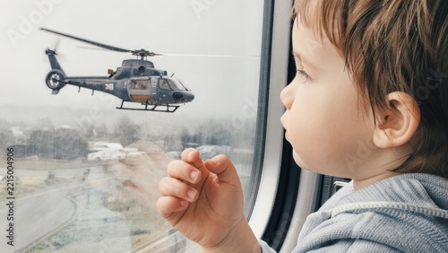 Child Watching Helicopter Through Airplane Window on a Cloudy Day