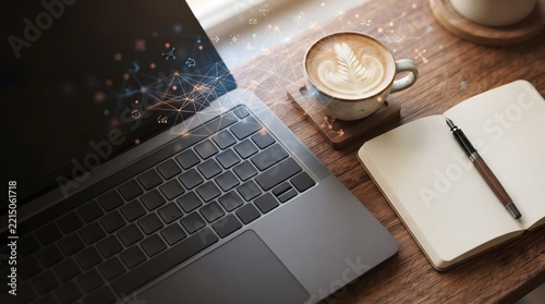 Close-up top view of laptop keyboard with latte coffee cup, notebook and pen on wooden desk