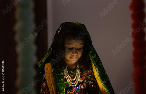 Portrait of a young Indian girl wearing traditional Gujarati ethnic clothing, she is looking down in warm cinematic lighting, creating a peaceful and elegant cultural portrait.