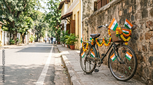 Vintage bicycle decorated with orange marigold garlands and small national flags parked beside a historic stone wall on a sunny urban street sidewalk