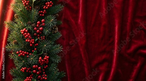 Christmas evergreen garland with red holly berries on soft red velvet background