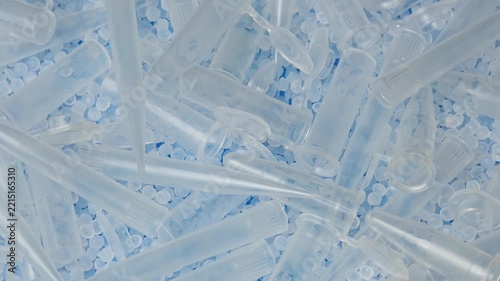 Clear centrifuge tubes and polymer pellets rotate together in close view for medical manufacturing.