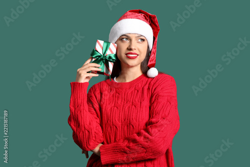 Happy young woman in Santa hat with gift box on green background. Christmas c...